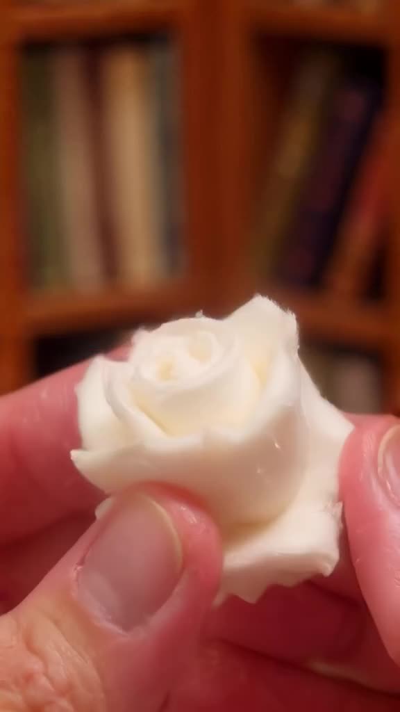 A realistic human hand made of soft, white clay slowly forms a perfect rose from thin air…