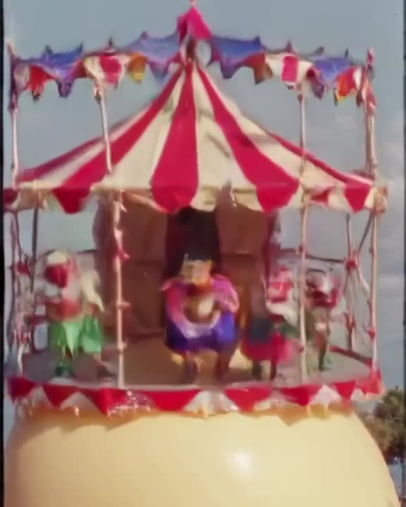 A miniature circus tent is set up on the lid of a giant pickled egg. Clowns jump onto the…
