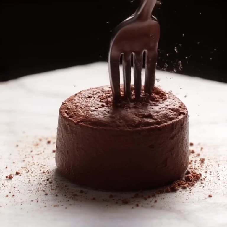 A giant molar made of dark chocolate sits on a white marble counter. A fork gently presse…