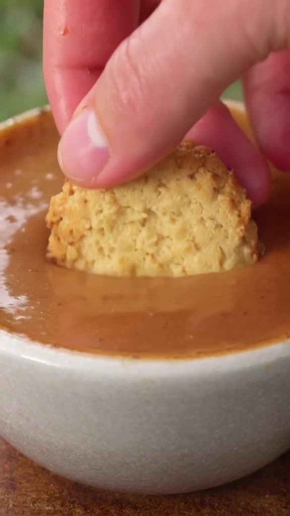 A hand dips a cookie into thick, glossy coffee. The cookie absorbs the liquid instantly, …