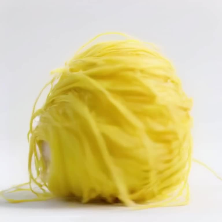 A ball of yellow yarn rolls across a white surface, morphing into a fluffy chick that wad…