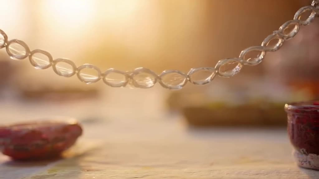A chain of wet, soapy glass tubes is pulled apart, stretching into long, thin strands tha…