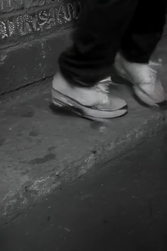 A pair of white sneakers executing complex footwork on a cracked concrete wall. Neon sign…