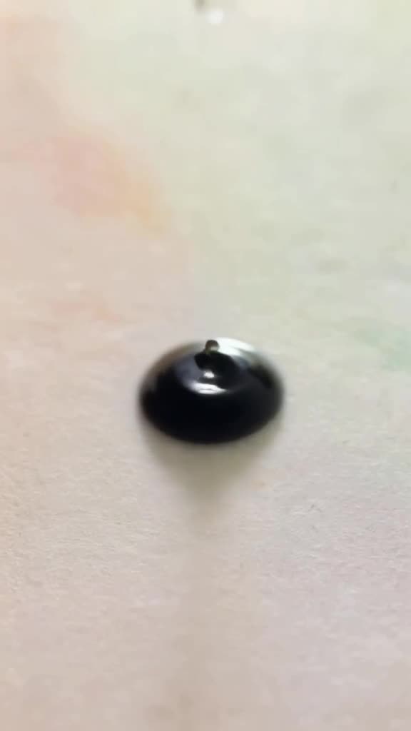 A single drop of milk falls into a pool of black espresso. The drop expands like a bloomi…