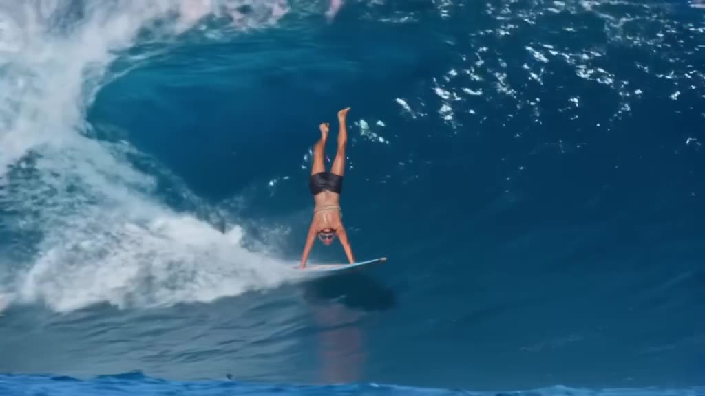 A grandma in oversized tortoiseshell sunglasses does a perfect handstand on a surfboard r…