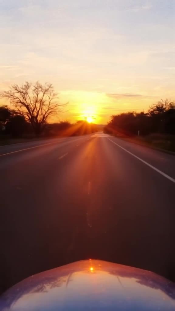 POV from a helmet visor looking at a sunset road. The horizon line suddenly ripples like …