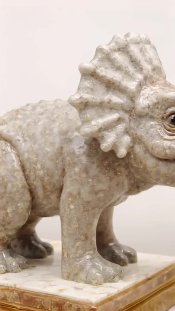 A miniature Triceratops made of polished marble slowly rotates on a velvet pedestal. Crac…