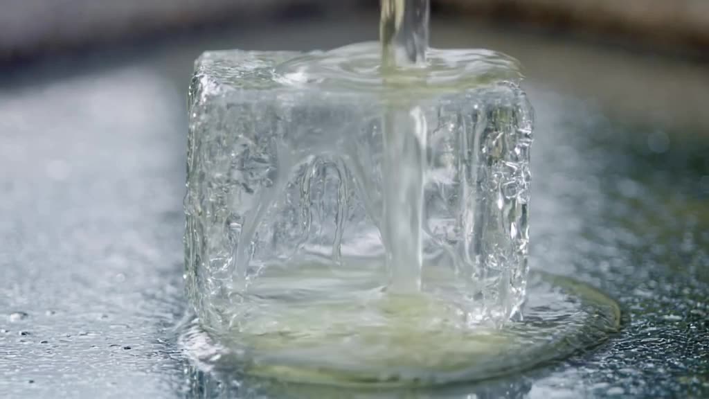 A crystal clear cube of ice sits on a mirror surface. Hot oil is poured over it, creating…