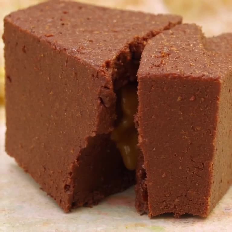 A piece of fudge is broken in half. The inside is not chocolate, but a flowing, molten go…
