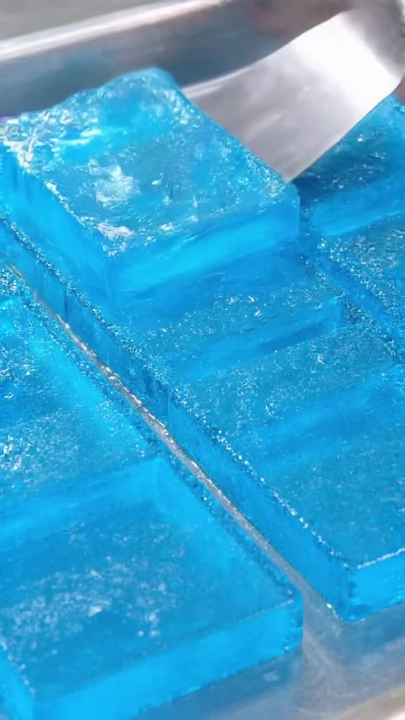 A row of ice cube trays shaped like seals are frozen in vibrant blue gelatin. A metal spa…