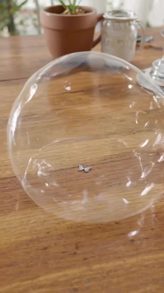 A soap bubble pops to reveal a tiny, perfect butterfly tattoo on a wooden table. Natural …