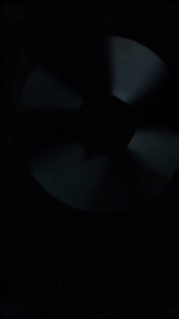 Dark, grainy VHS footage of a computer fan spinning faster and faster. Suddenly, the fan …
