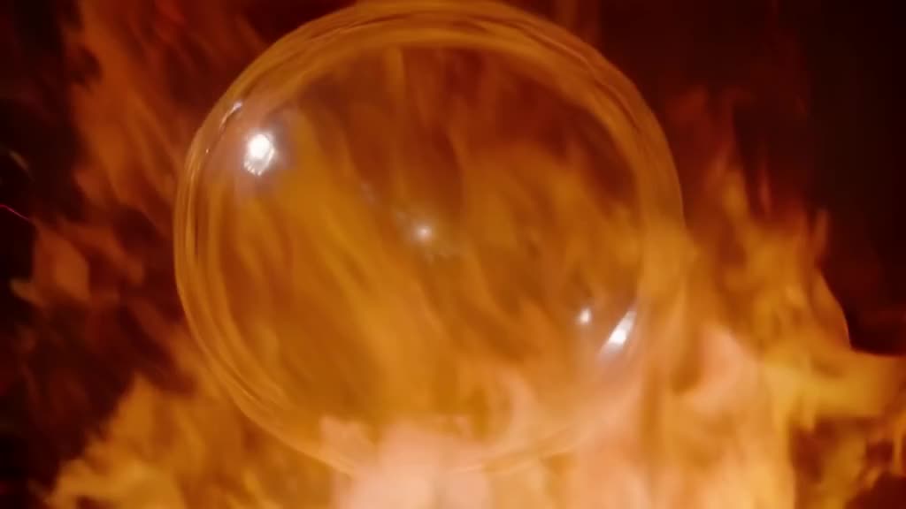 Extreme close-up of a molten glass bubble being inflated by a tiny breath. The bubble str…