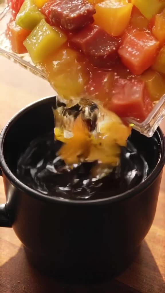An ice cube tray filled with colorful fruit puree cubes is dropped into black coffee. Eac…