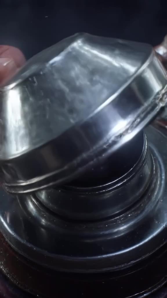 A vintage car’s fuel cap opens to reveal a tiny, glowing galaxy inside. The cap is chrome…