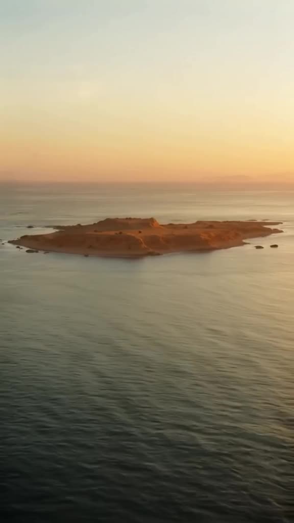 A drone shot of a desert island made entirely of stacked coins. The camera swoops down to…
