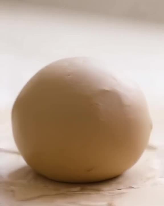 A perfect sphere of clay is rolled on a table, shrinking perfectly into a ball. Smooth, c…