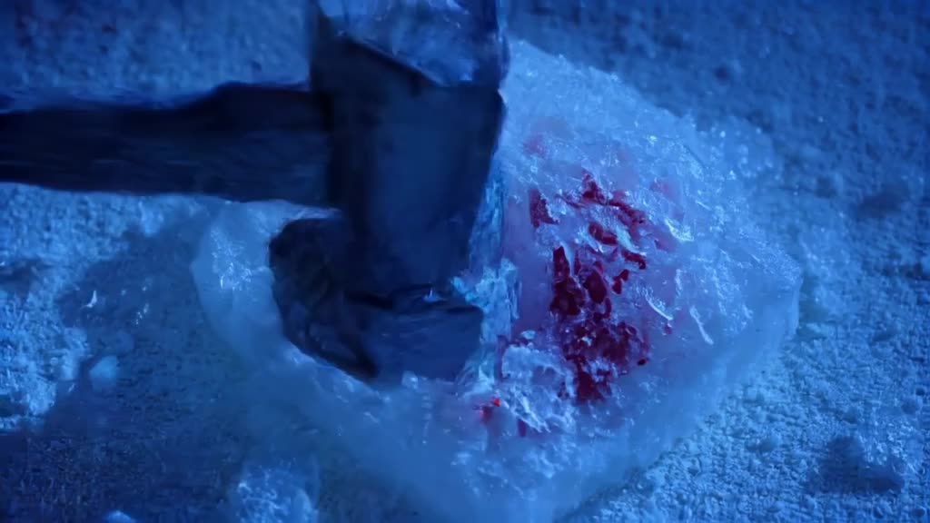 A block of ice containing frozen flowers is crushed by a hammer, revealing red roses insi…