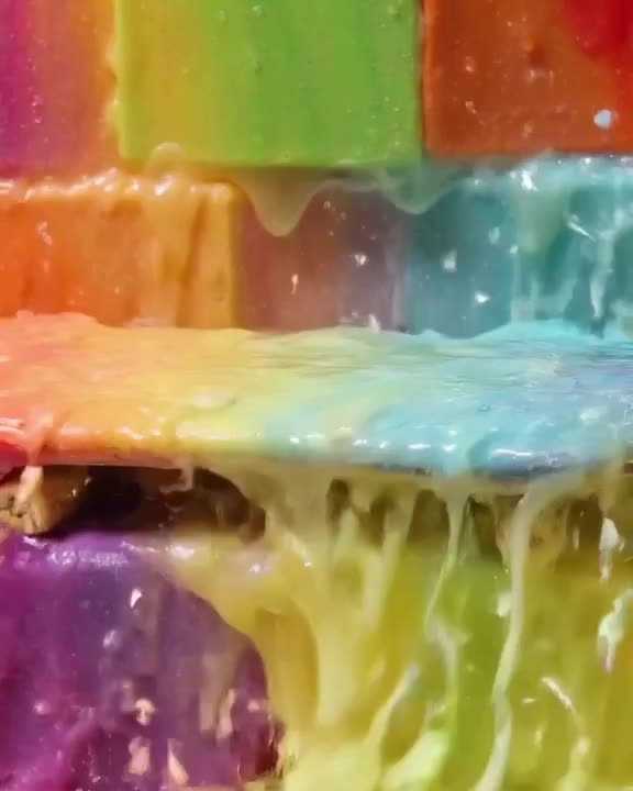 A skateboard sits on a surface of rainbow-colored, gelatinous blocks. A hammer strikes th…