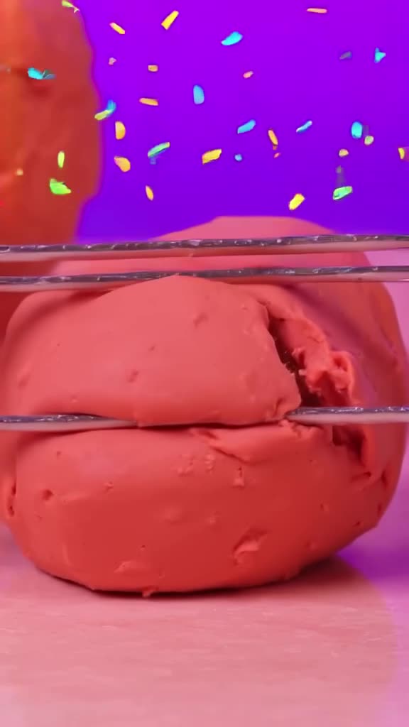 A ball of playdough is sliced with a wire cutter, revealing a hidden glittery core. Confe…