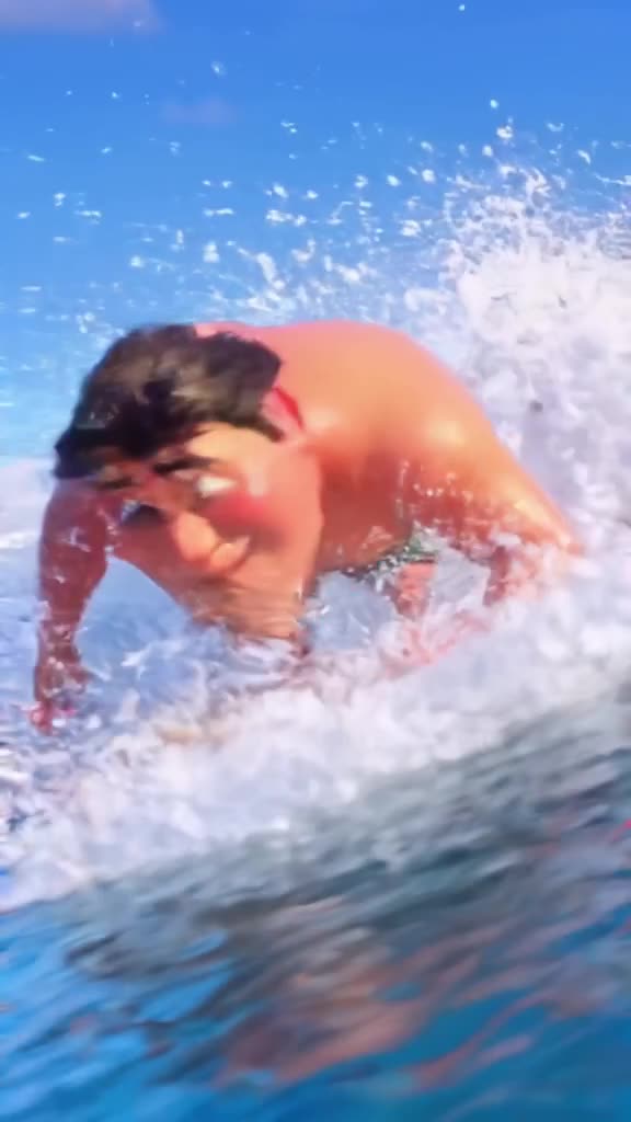 A senior man surfing on a wave made of whipped cream and sprinkles, licking his lips with…