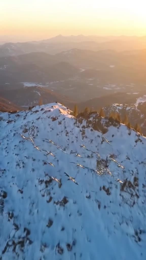 Drone shot: a flock of toy birds flies in formation over a snowy mountain range. They spi…