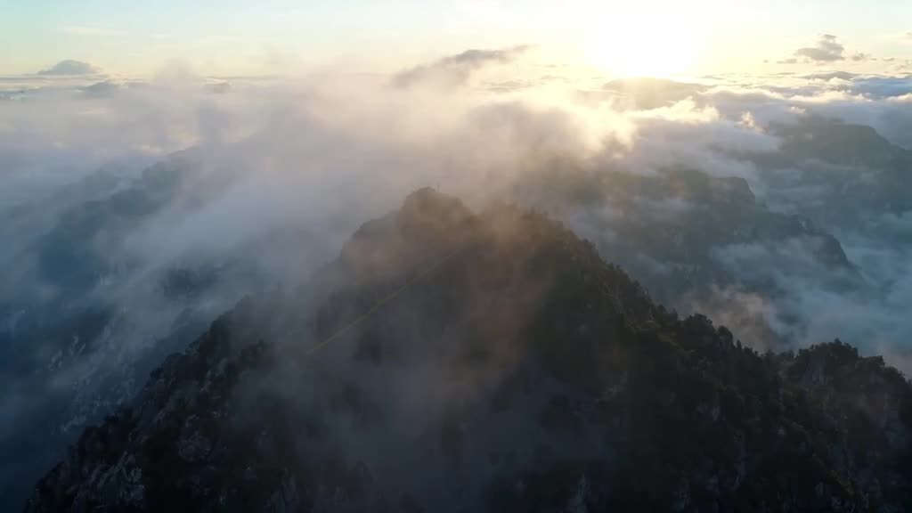 Misty Swiss Alps peaks pierce through soft clouds. A giant needle stitches a tear in the …