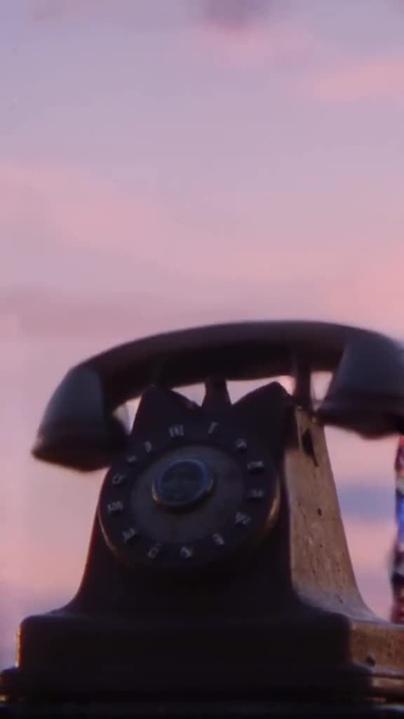 A vintage rotary phone dial spinning as soapy bubbles emerge from the earpiece, floating …