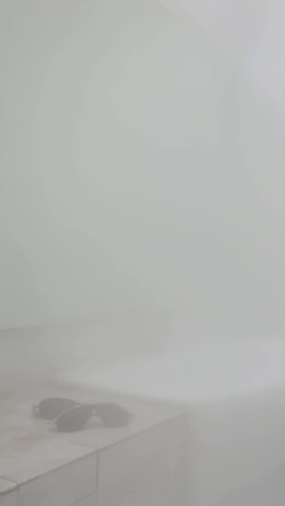 Minimalist white bathroom, foggy mirror, sunglasses placed neatly on a tiled edge, soft d…