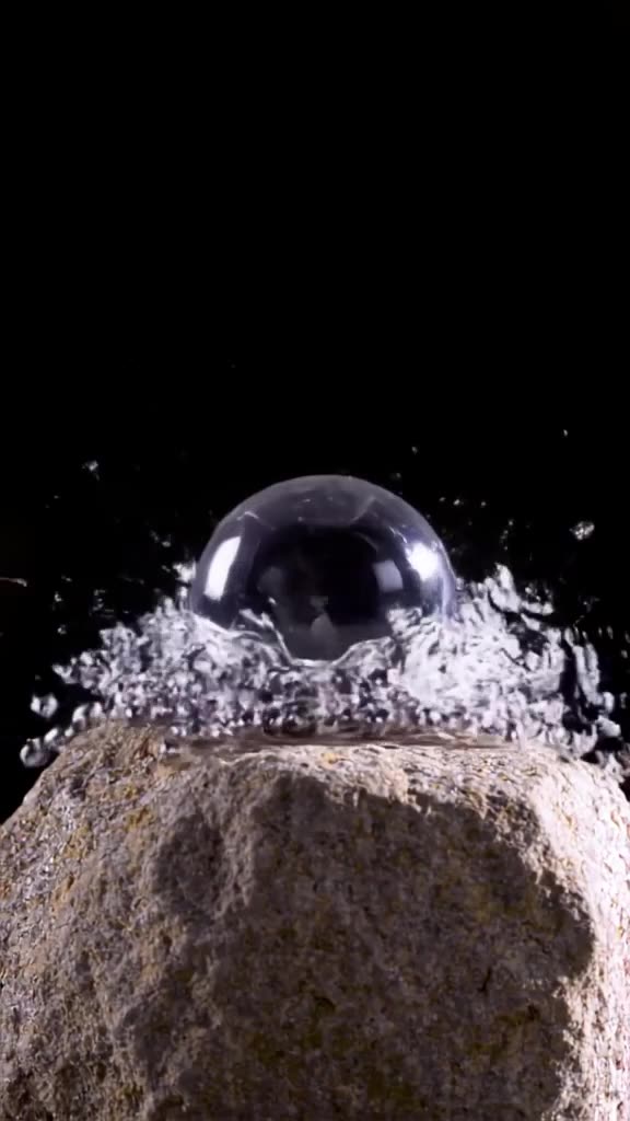 A perfect sphere of liquid mercury rolls over a rough stone surface, shattering into doze…