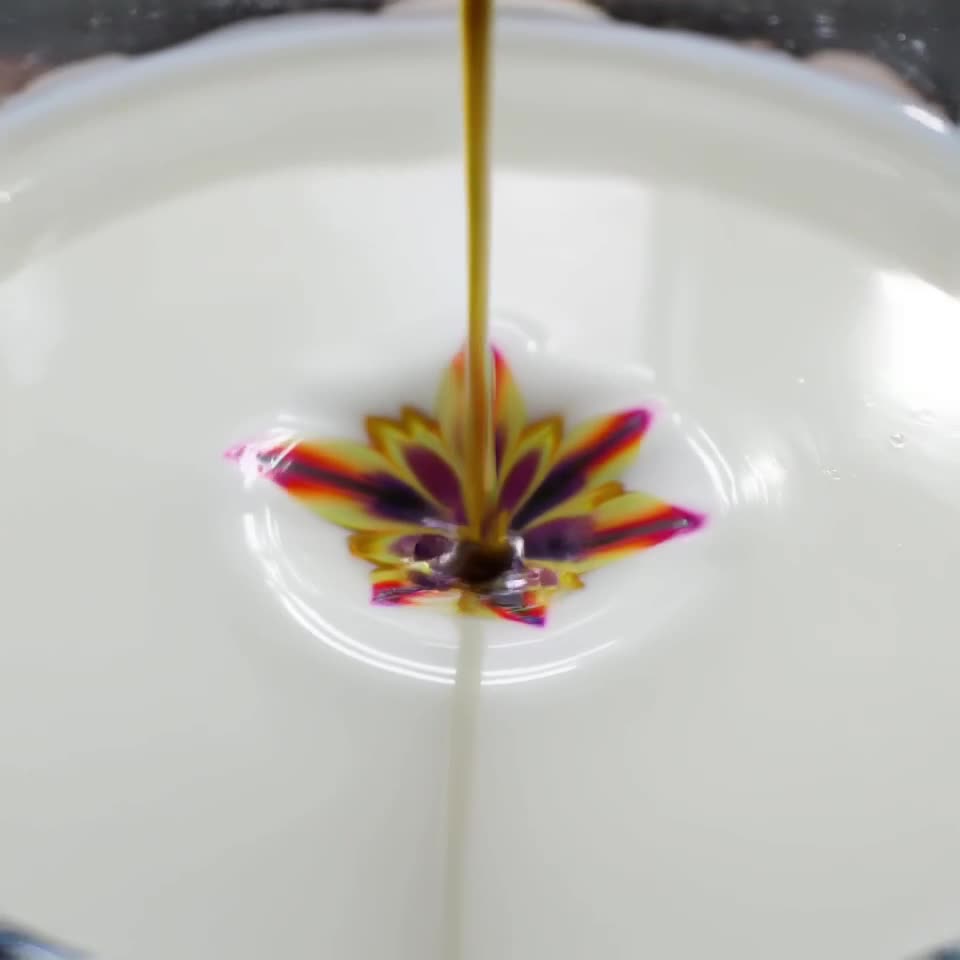 A single drop of food coloring falls into a glass of milk, creating intricate, flower-lik…