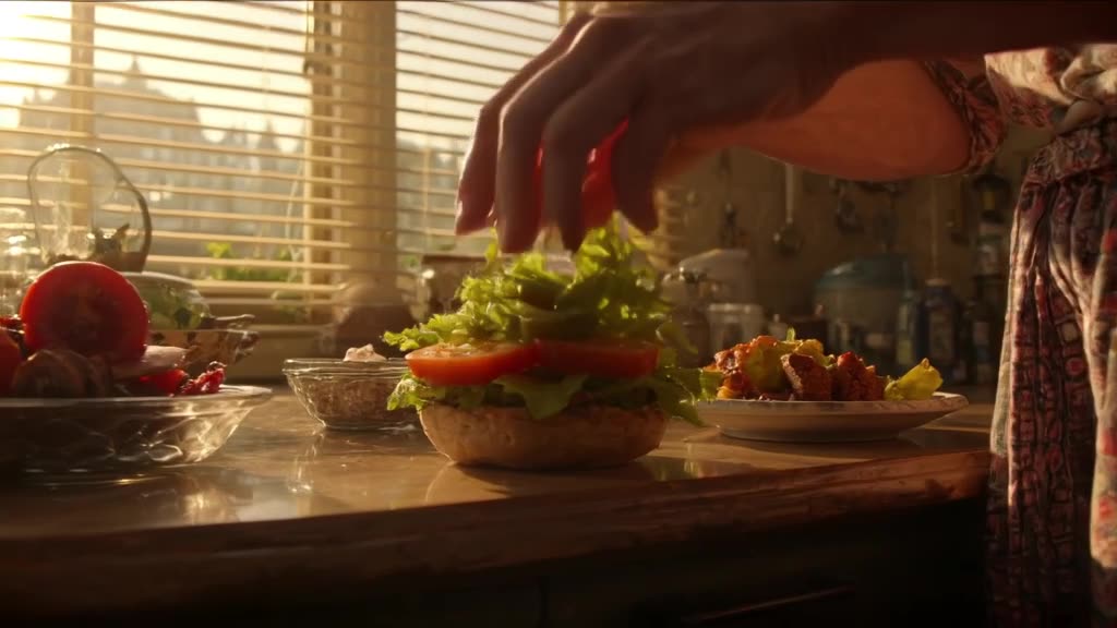 Close-up of a burger being assembled on a vintage kitchen counter. Hands drop crispy lett…