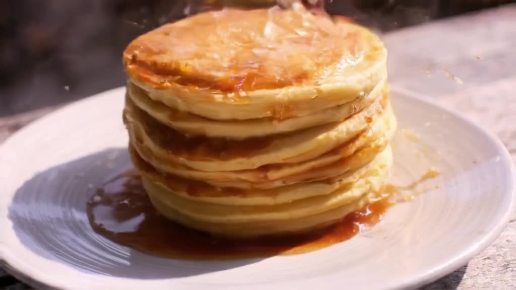 A stack of pancakes flips itself in the air, landing perfectly on a plate with syrup spla…