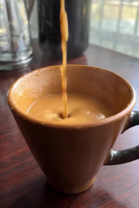 A zombie barista pours latte art into a cup of thick, opaque brown coffee. The milk forms…